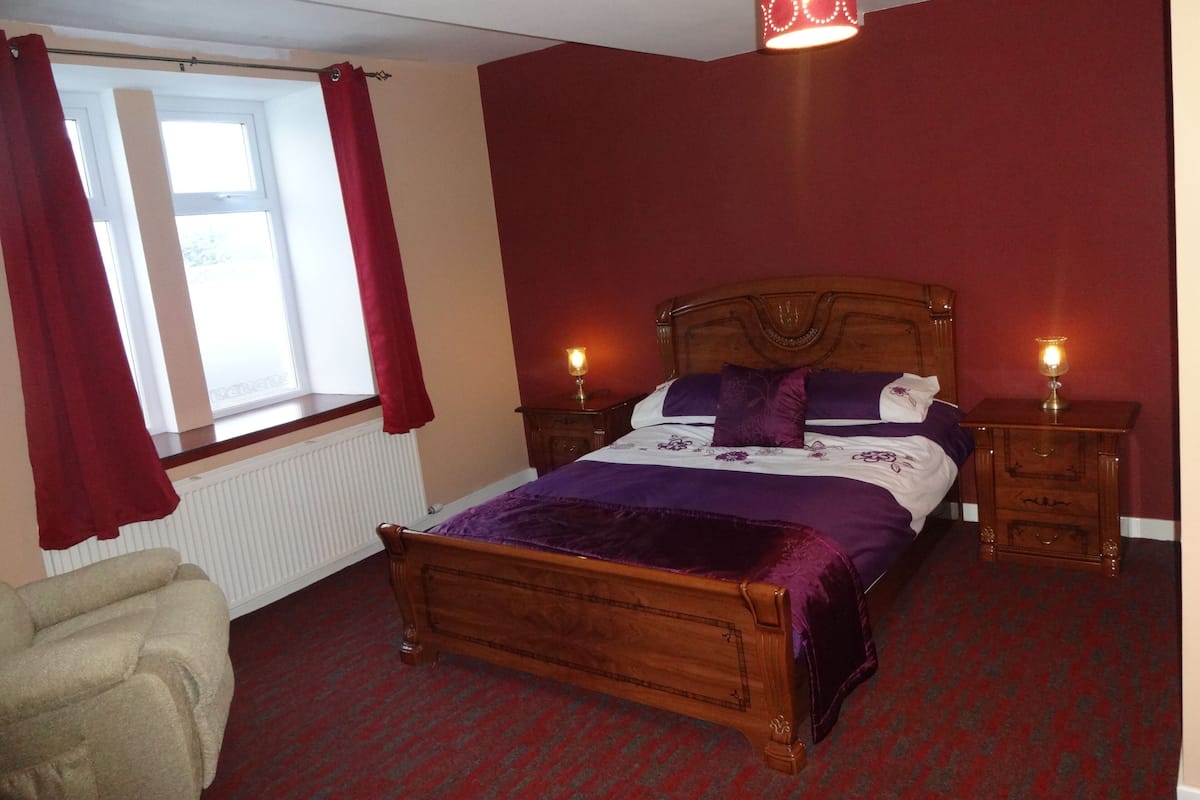 A bedroom with a wooden bed, red curtains, a red carpet, and two bedside lamps.