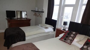 A bedroom with two beds, a dresser, a TV, and a window with a view.