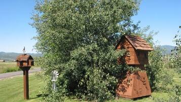 A rustic wooden structure with a sloped roof, surrounded by lush greenery and a clear sky.