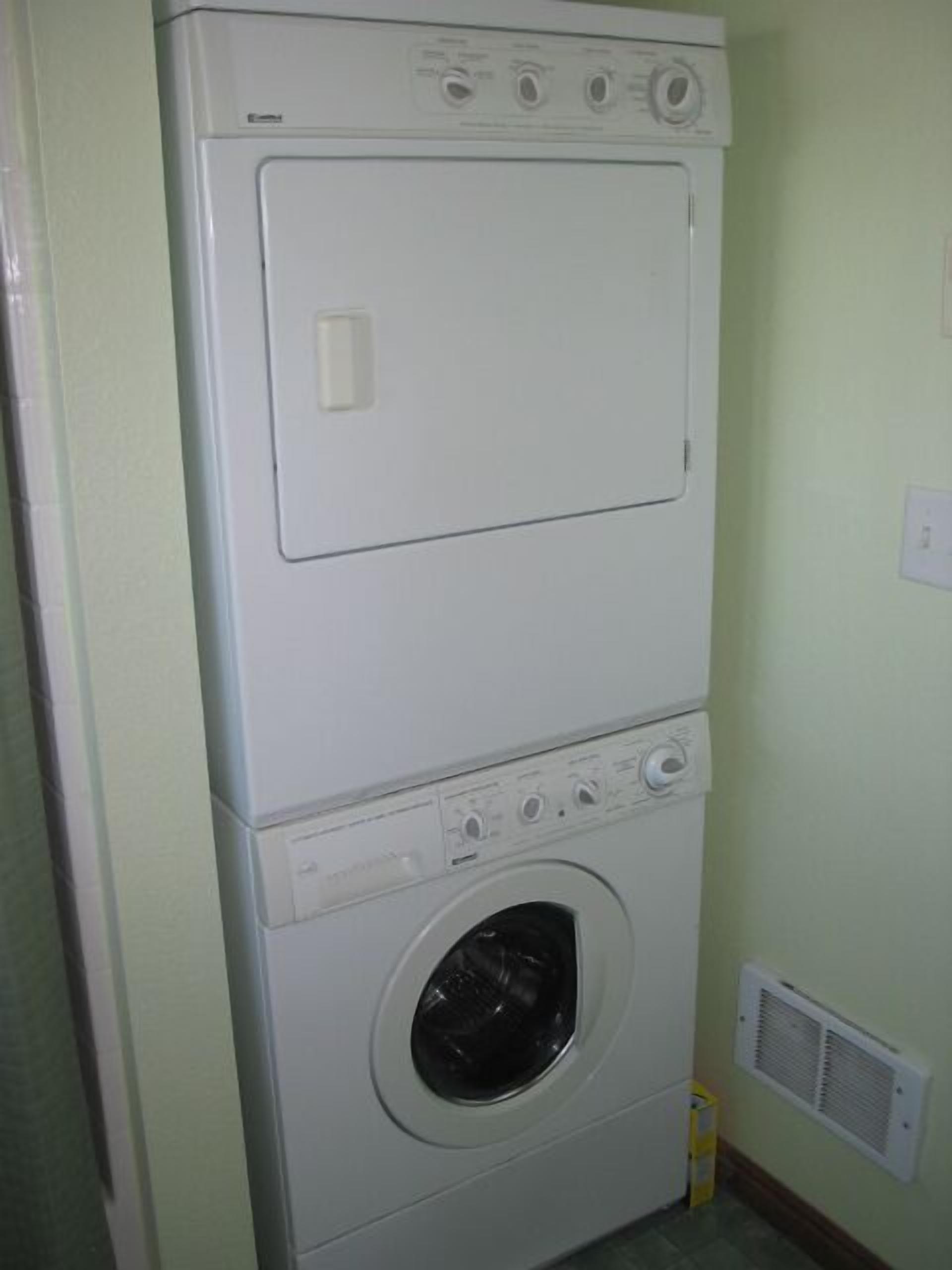 A stacked washer and dryer unit in a room with light green walls and a vent on the wall.