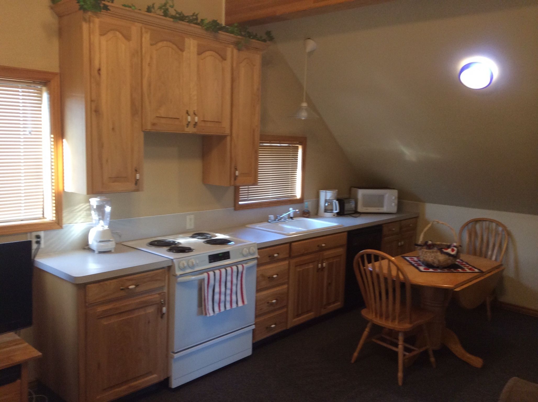A compact kitchen with wooden cabinets, a stove, a microwave, and a dining area with a table and chairs.