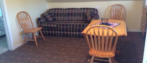 Ein Wohnzimmer mit einem karierten Sofa, zwei Holzstühlen, einem kleinen Tisch und einem gerahmten Bild an der Wand.