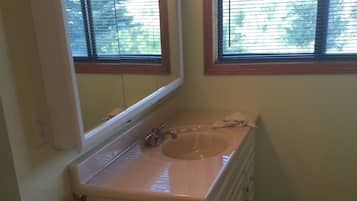 A small bathroom with a sink, mirror, and window.