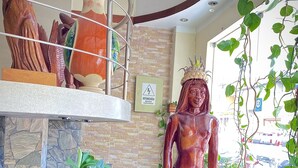 Estátua de uma figura com coroa, cercada por vegetação e um aviso de risco elétrico.