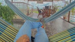 Uma pessoa relaxando em uma rede em área externa coberta, com vista para o céu e plantas.