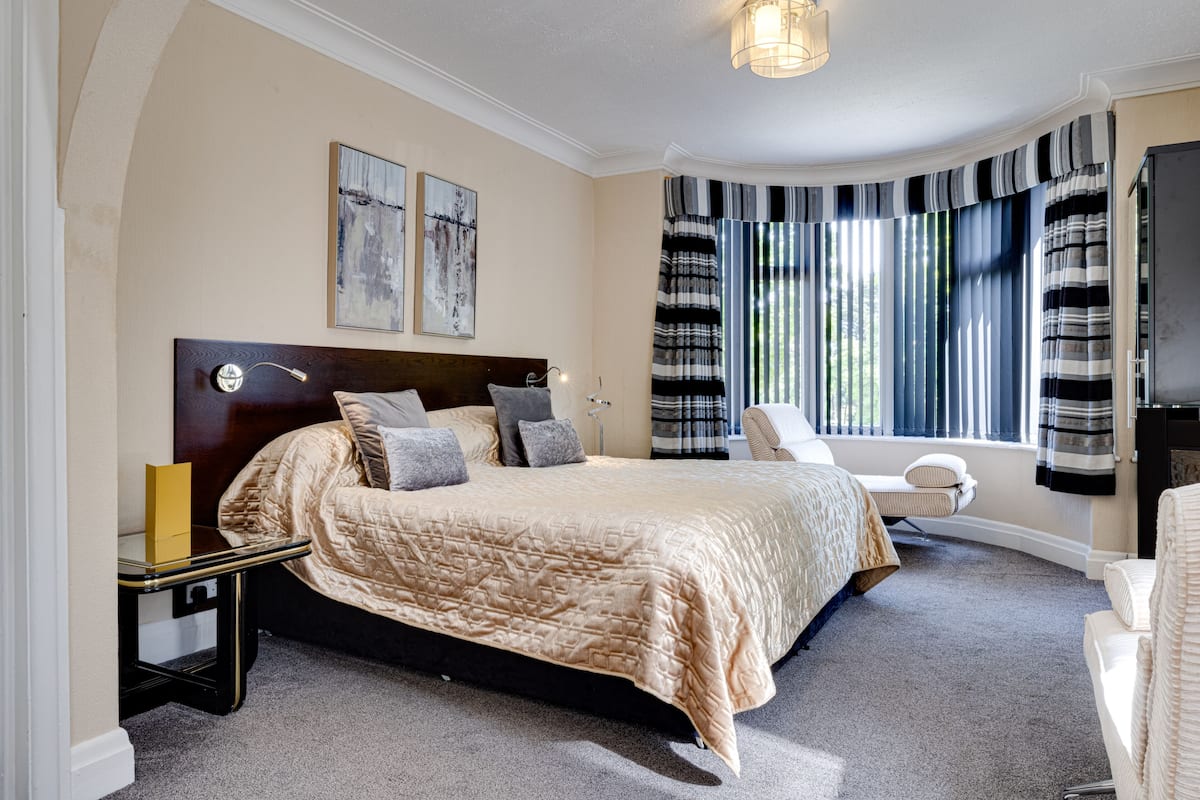 A bedroom with a large bed, a bedside table, a chair, a TV, and a window with curtains.