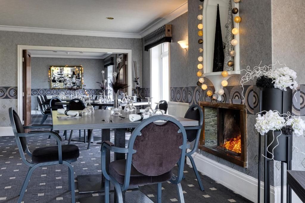 A dining area with a long table, chairs, a fireplace, and a mirror with lights.