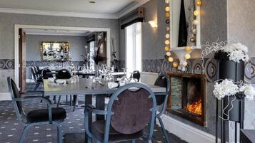 A dining area with a long table, chairs, a fireplace, and a mirror with lights.
