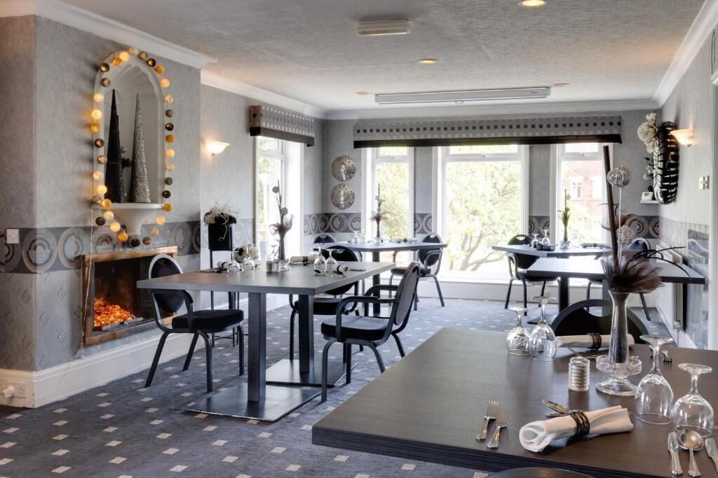 Un espace de salle à manger moderne comprenant deux tables, des chaises, une cheminée et des appliques murales décoratives.