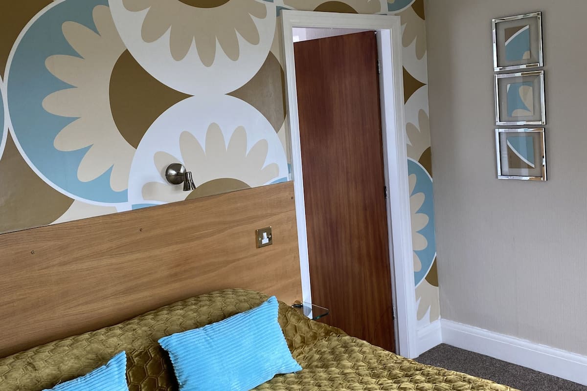 A bedroom with a bed, a wooden headboard, a patterned wall, a door, and three framed pictures on the wall.