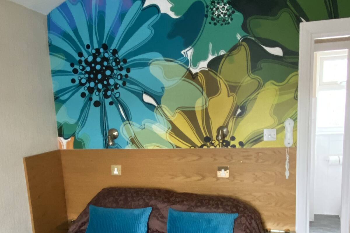 A bedroom with a floral-patterned headboard, a brown bedspread, and two blue pillows.