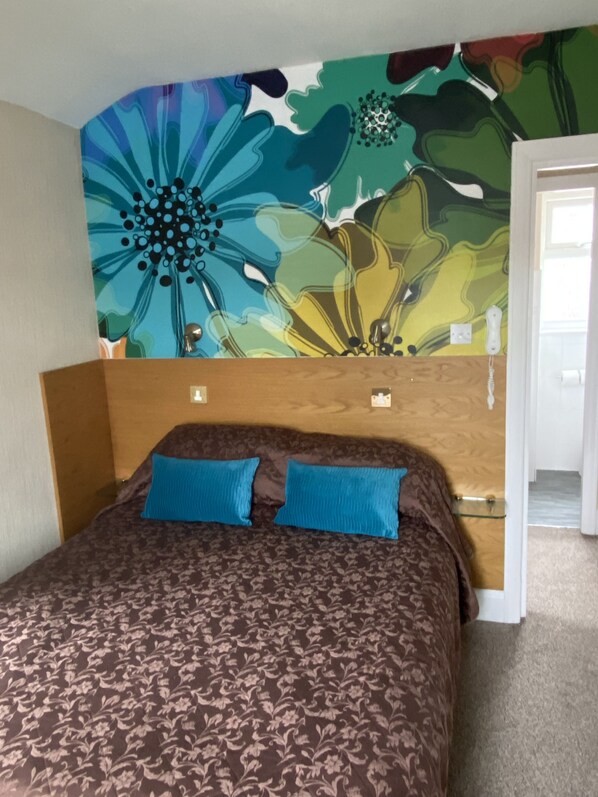 A bedroom with a floral-patterned headboard, a brown bedspread, and two blue pillows. - Park Manor Hotel (Scarborough)
