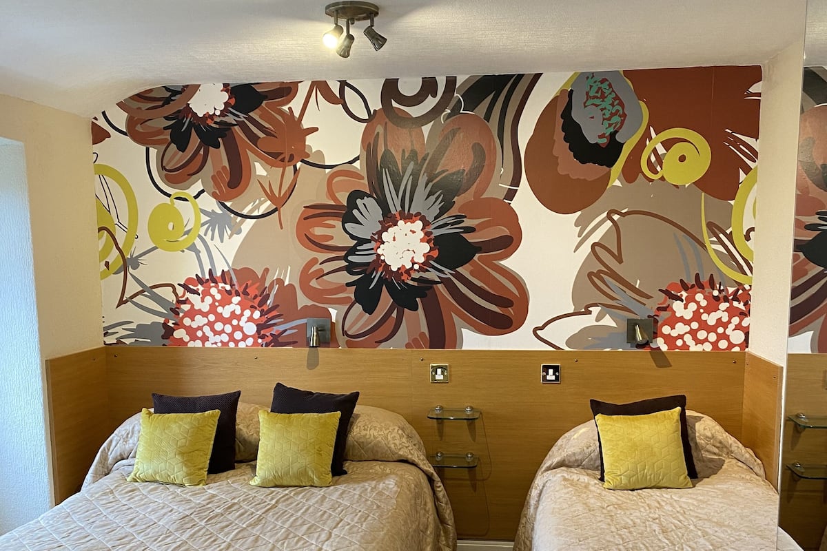 A hotel room with two beds, a floral wall mural, and a ceiling light fixture.