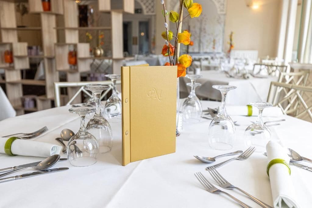 A restaurant setting with tables set for dining, featuring clear glassware and a menu stand.