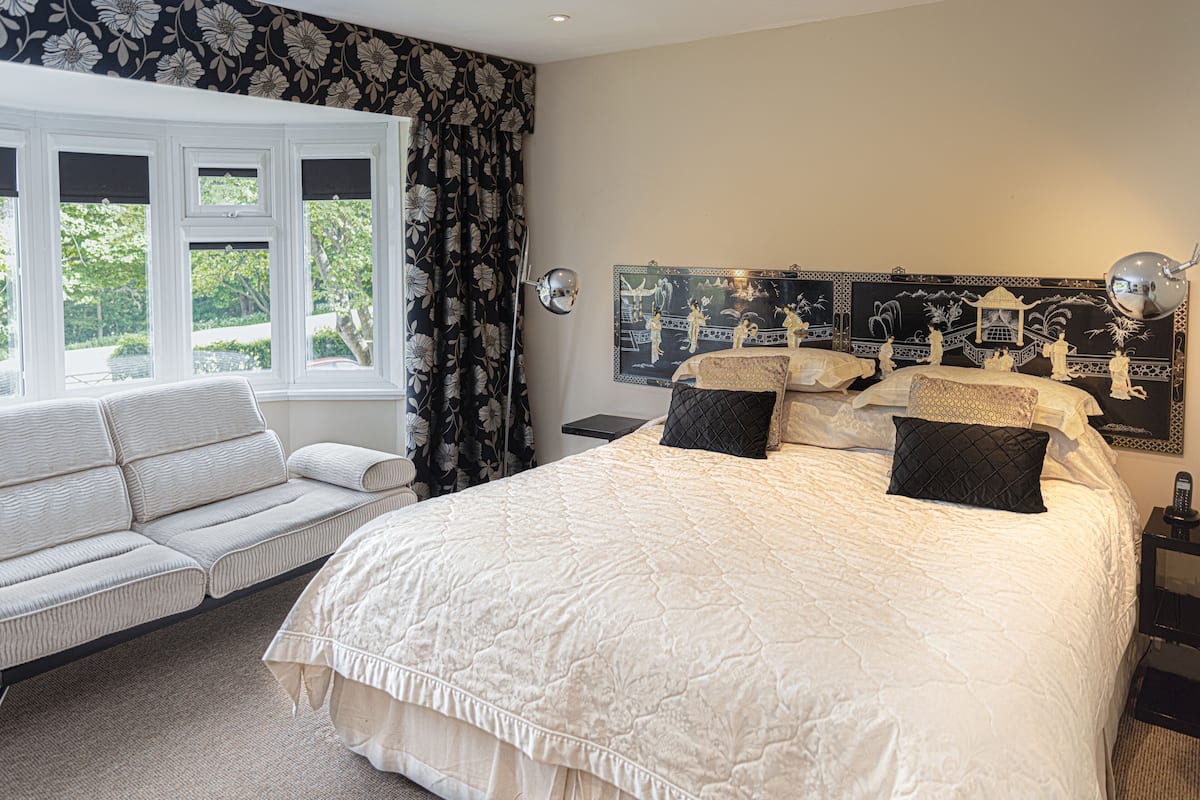 A bedroom with a large bed, a sofa, a mirror, and a window with curtains.