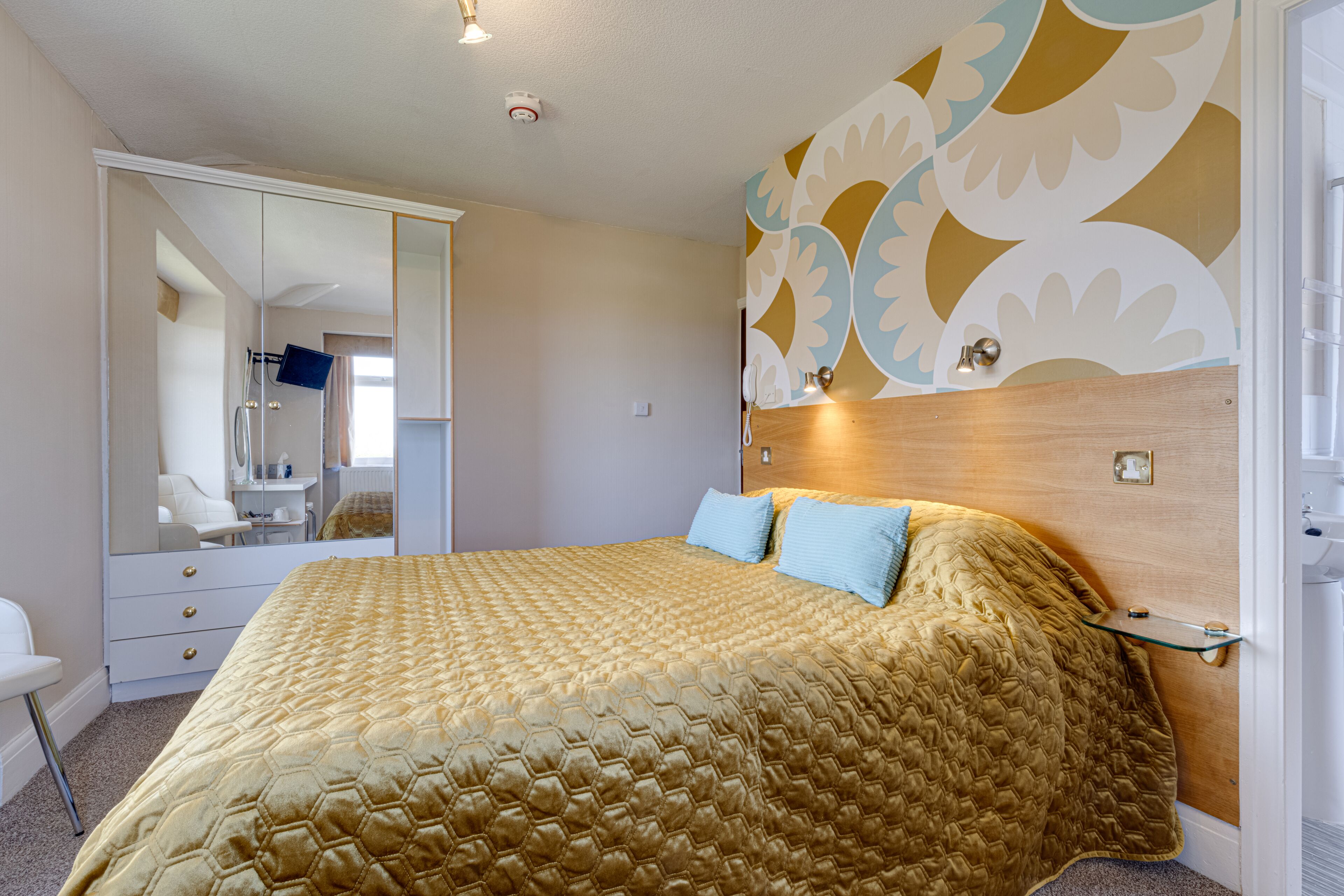Une chambre d’hôtel avec un grand lit, une armoire, un miroir et un mur décoratif.