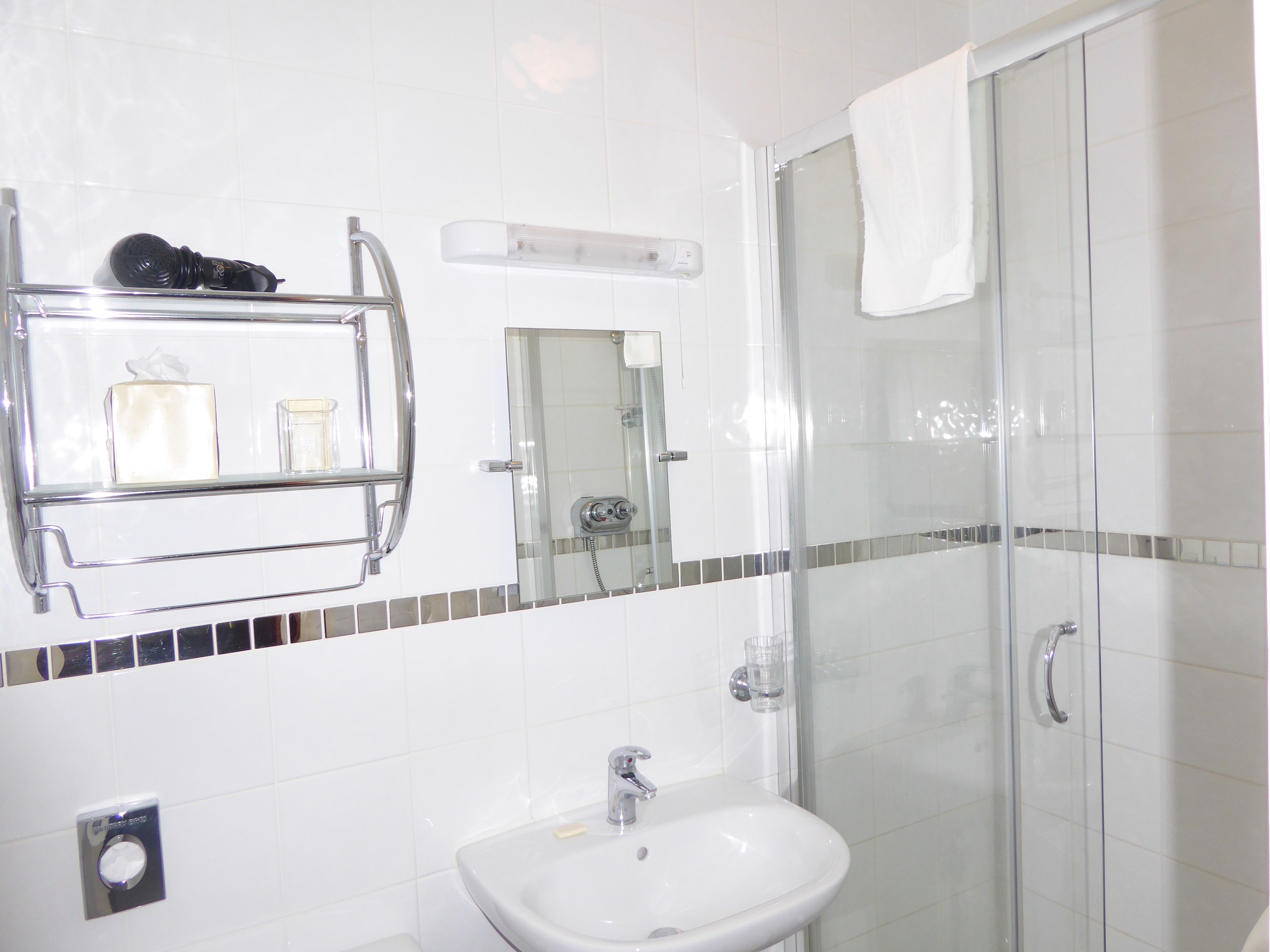 A bathroom with a glass shower enclosure, a sink, a mirror, and a towel hanging on the shower door.