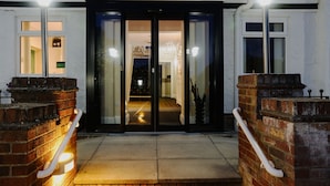A hotel entrance with a glass door, a brick wall, and a light fixture. - Park Manor Hotel (Scarborough)