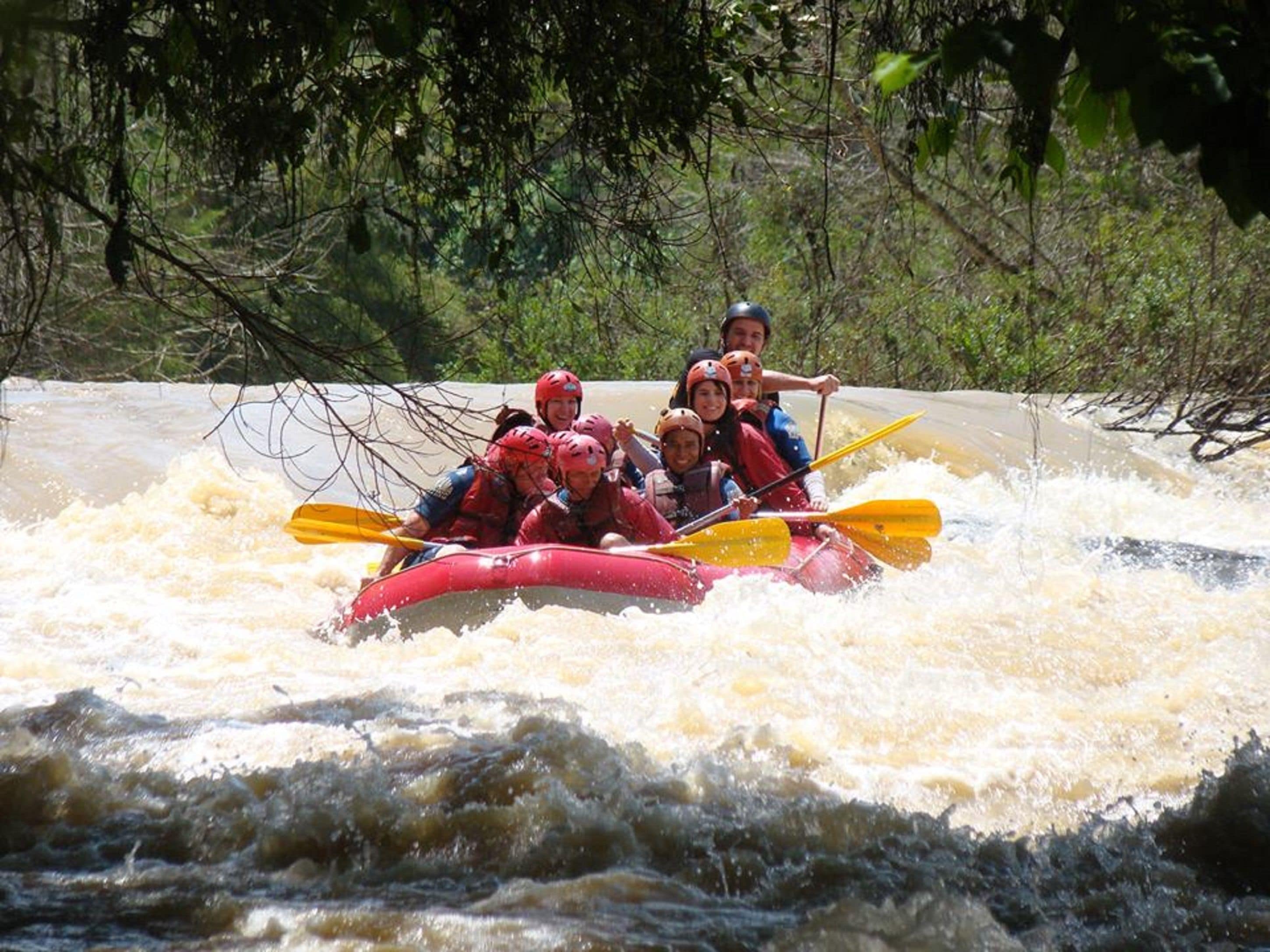 A group of people in a red raft navigating through a river with rapids.