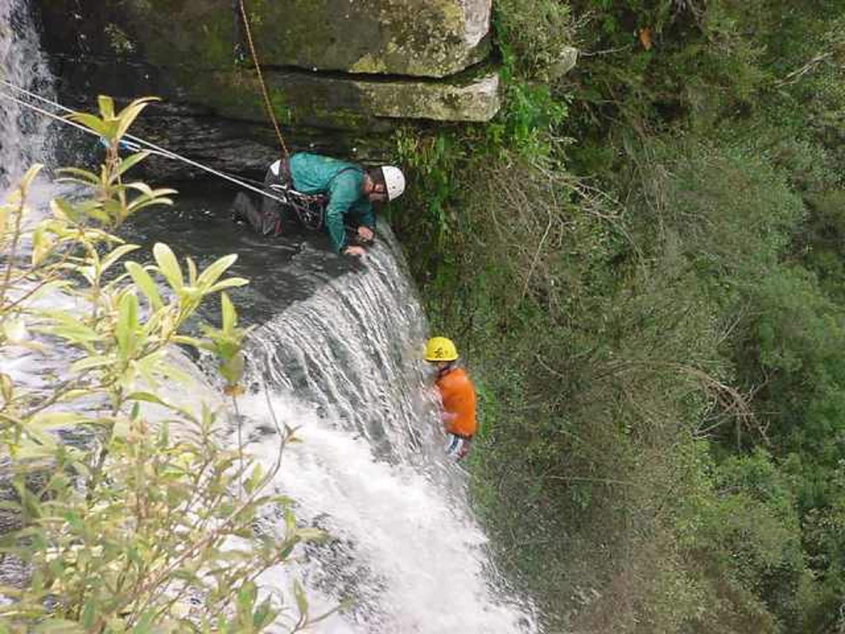 A person rappelling down a waterfall with a rope.