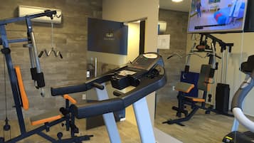 A gym with exercise equipment, a TV, and a mirror.