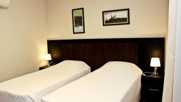 Habitación de hotel con dos camas individuales, cabecero de madera, lámparas de noche y dos cuadros en la pared.