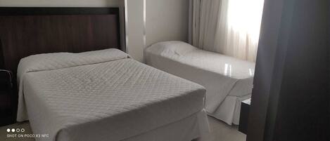 A hotel room with two beds, a dark wooden headboard, and a window with curtains.