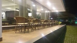 Un edificio moderno con una hilera larga de sillas de madera afuera, un muro de vidrio y un interior bien iluminado.