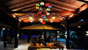 Un espace extérieur abrité, doté d’un plafond en bois, d’une table centrale et de guirlandes lumineuses décoratives.