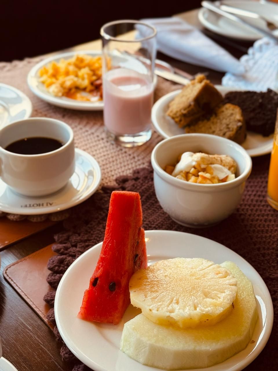 Une table mise pour le petit-déjeuner, avec des assiettes remplies de nourriture, un verre d’une boisson rose et une tasse de café noir.