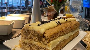 A slice of layered cake on a white plate, with a dark lamp and decorative lights in the background.