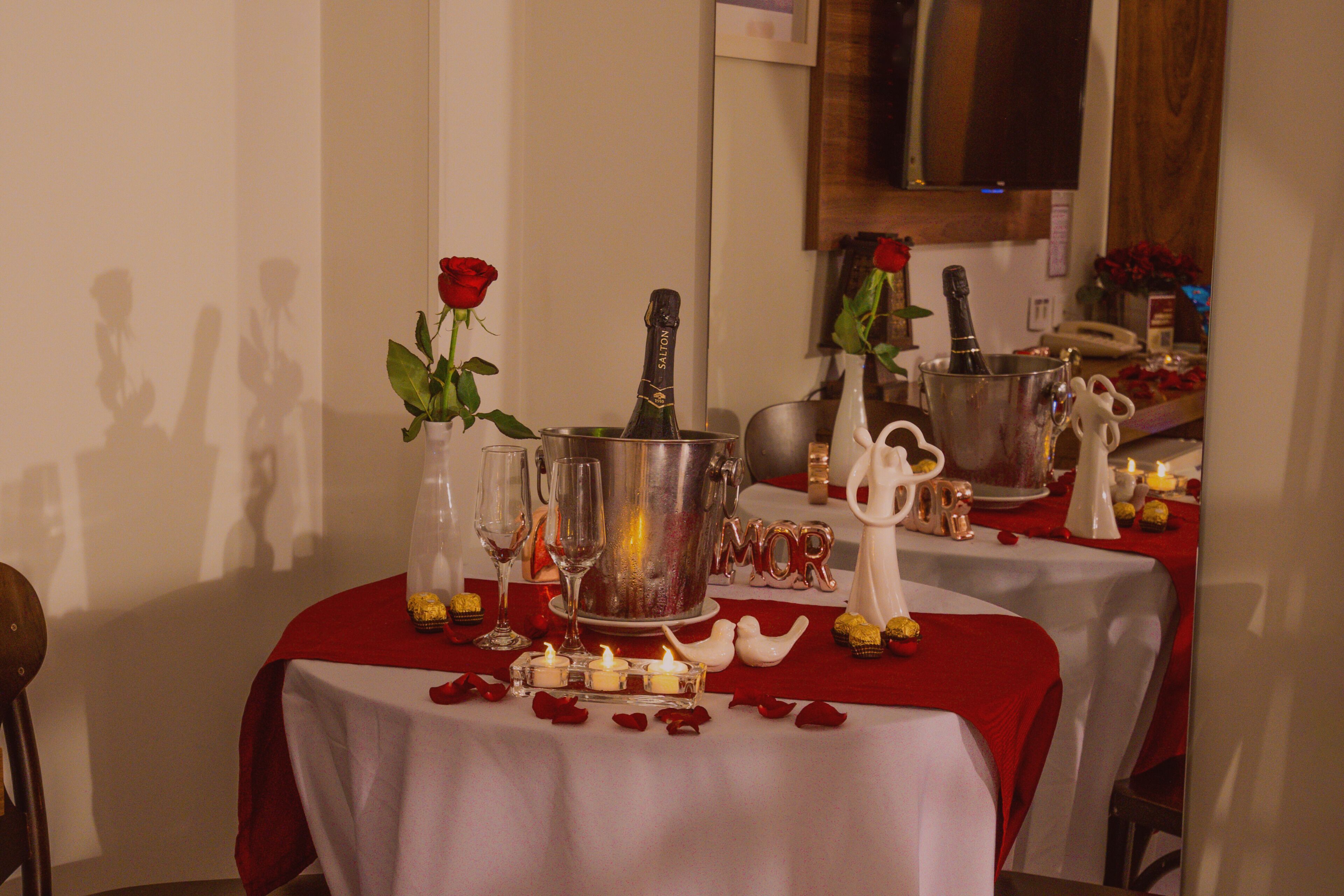 A table set for a romantic dinner with champagne, roses, candles, and a 'MOR' sign.
