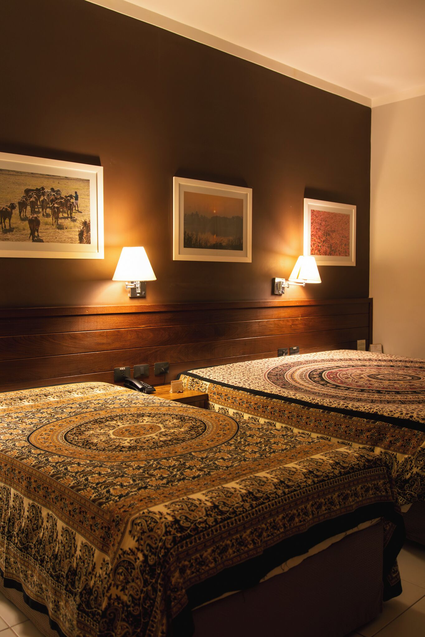 A hotel room with two beds, a wooden headboard, wall-mounted lamps, and framed artwork.