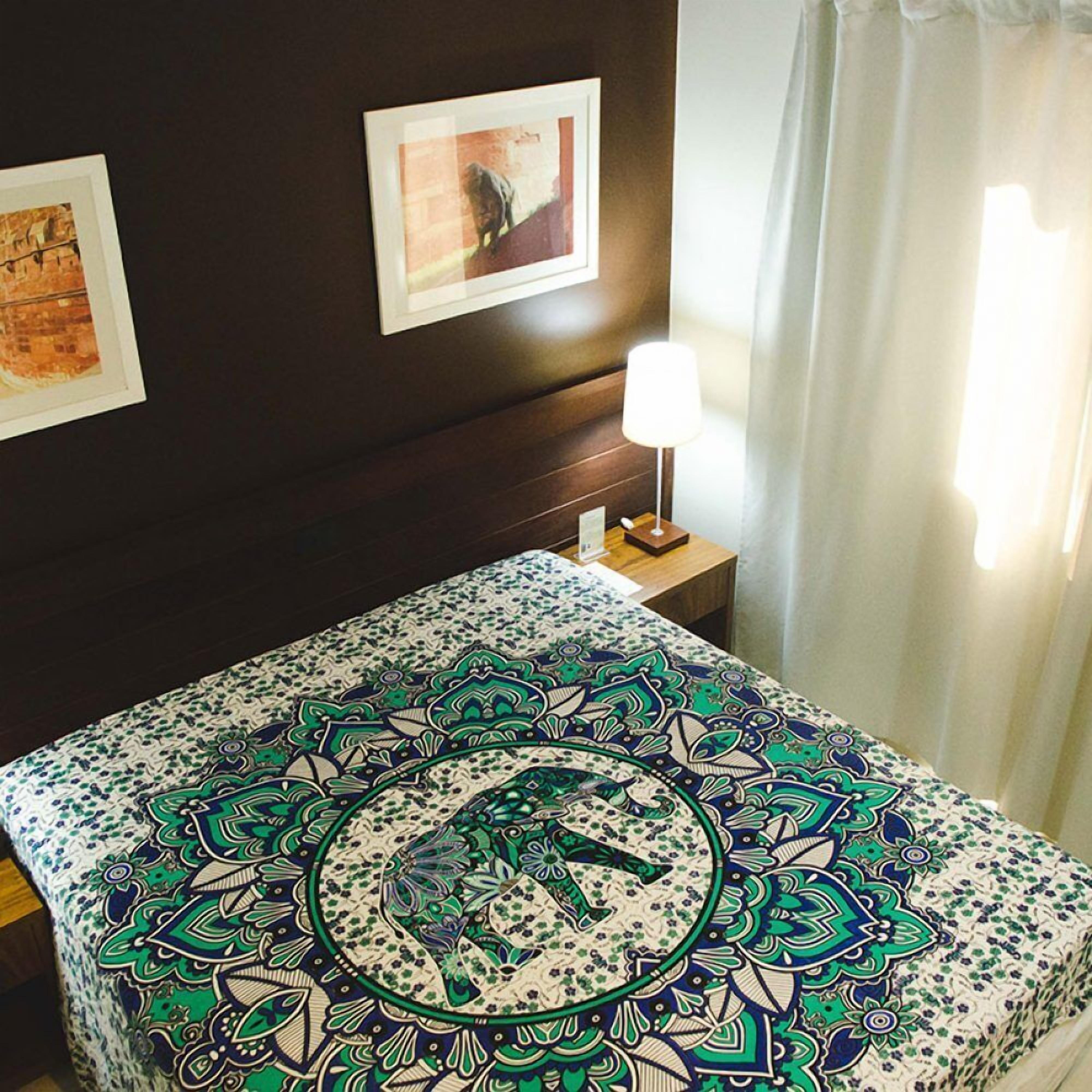 A hotel room with a patterned bedspread, a nightstand with a lamp, and two framed pictures on the wall.