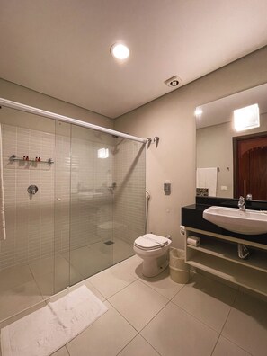 Une salle de bain moderne avec une douche à parois de verre, des toilettes blanches, un lavabo doté d’un plan de travail noir et un miroir au-dessus du lavabo.
