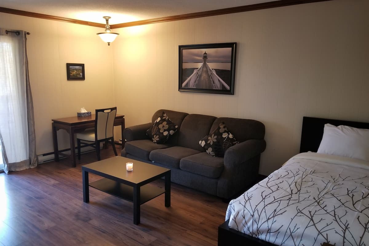 A hotel room with a wooden floor, a sofa, a small table, a bed, a desk, and a picture on the wall.