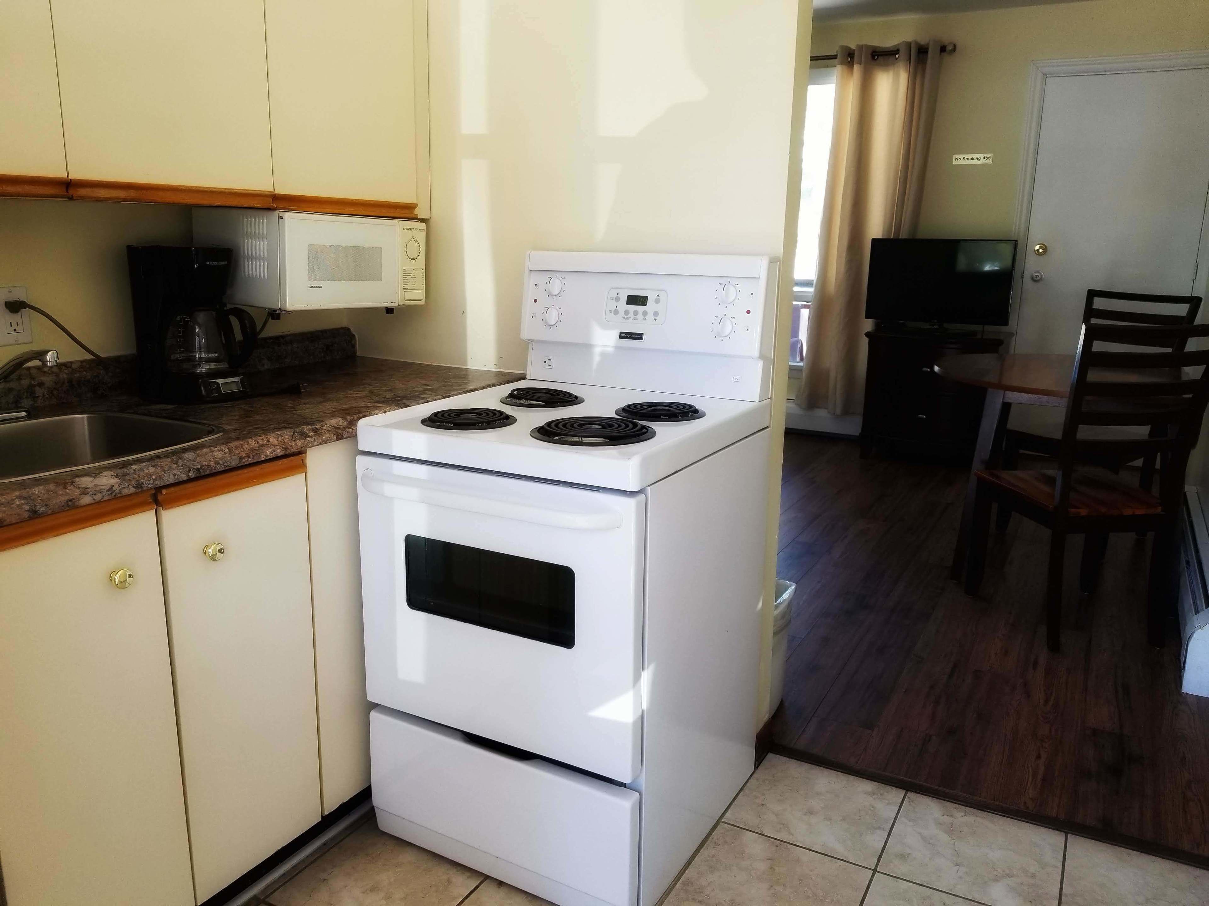 A compact kitchen with a white stove, a microwave, and a coffee maker. There is a dining area with a table and chairs.