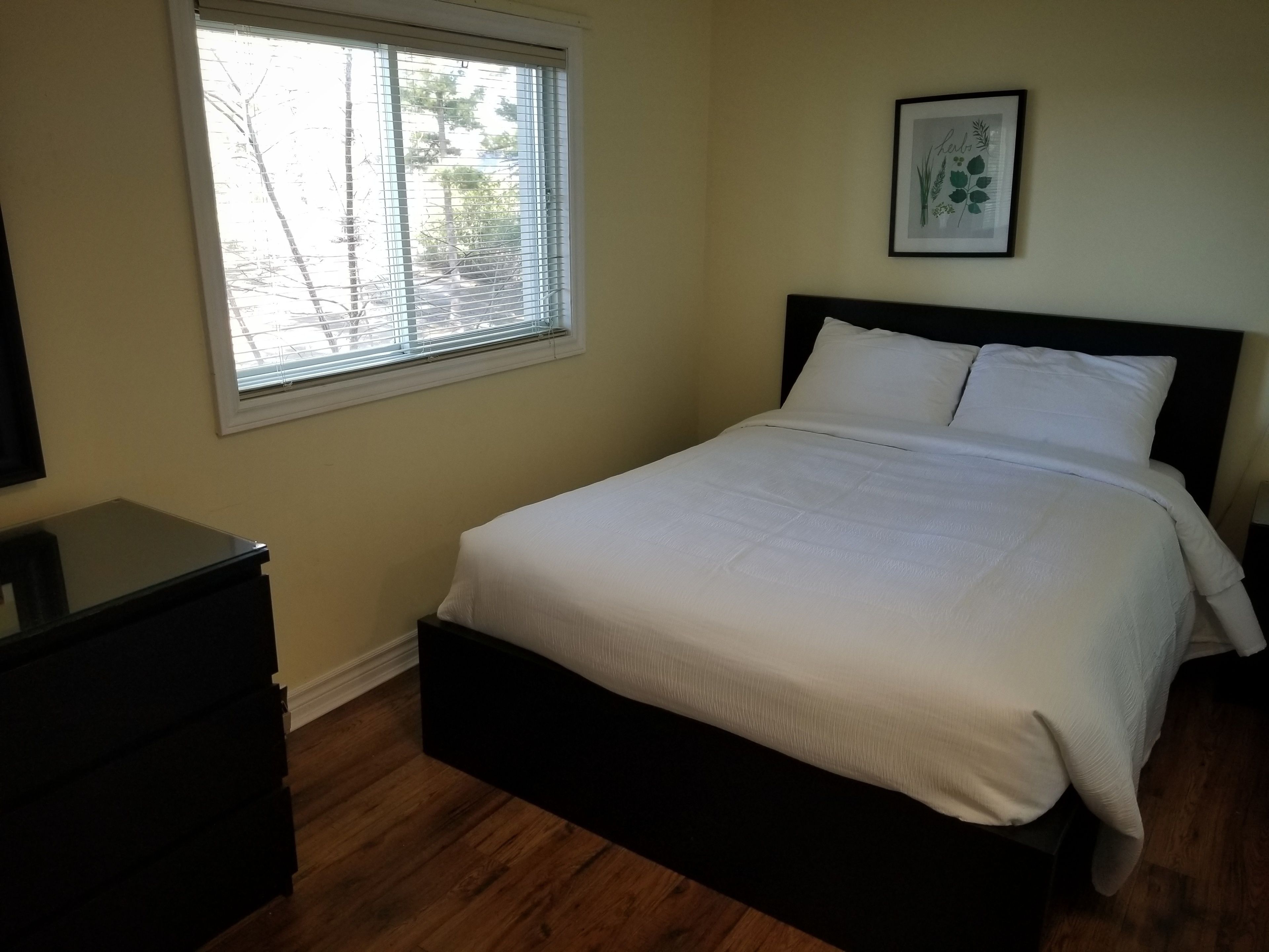 Un dormitorio con cama, cómoda, ventana y un cuadro en la pared.