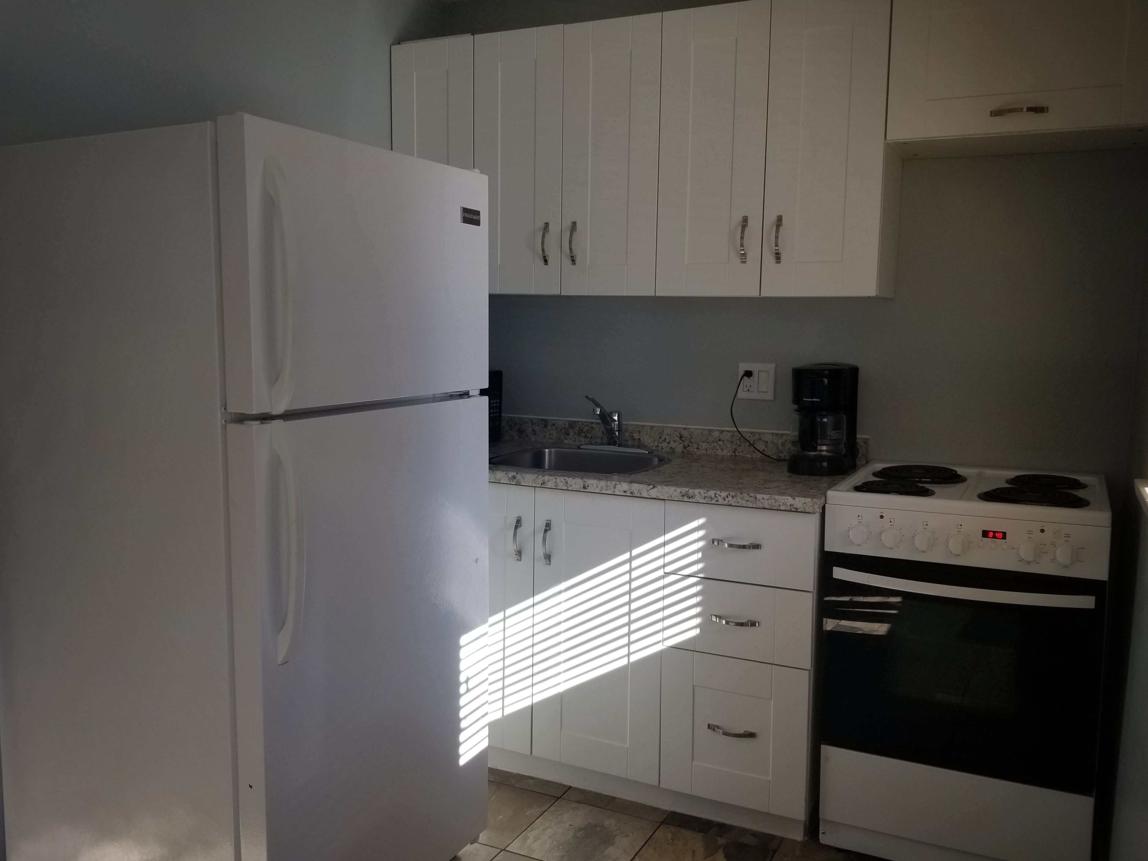 A compact kitchen with white cabinets, a white refrigerator, a sink, a coffee maker, and a stove.