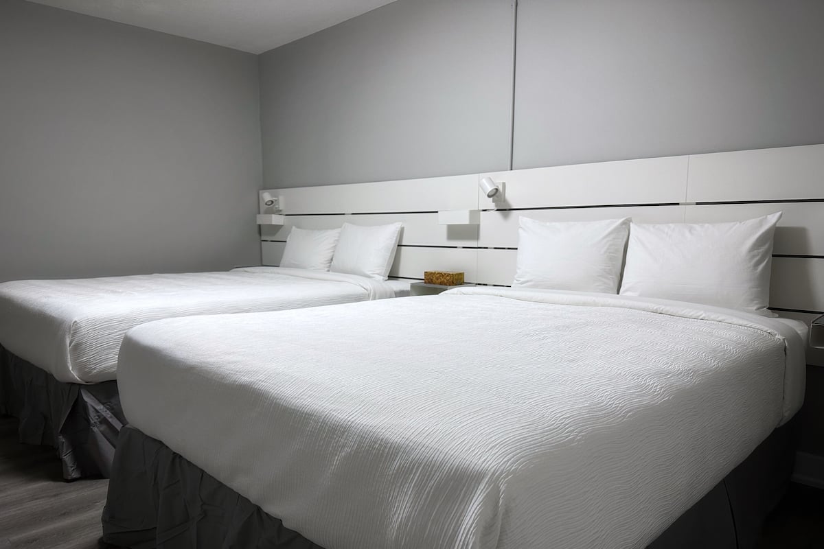 A hotel room with two beds, each with white bedding and a headboard with a light switch.