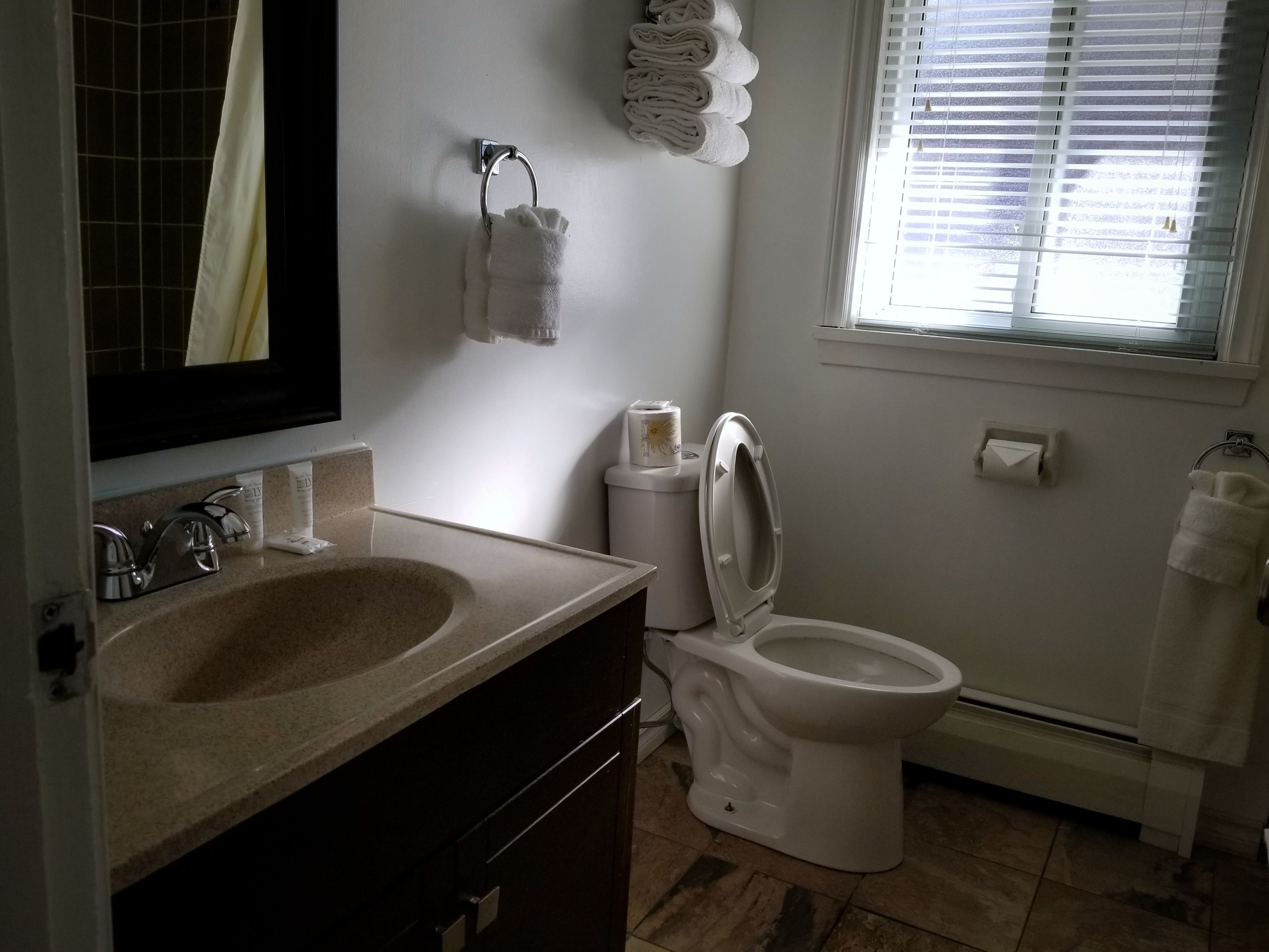 A bathroom with a sink, toilet, and a window with blinds.