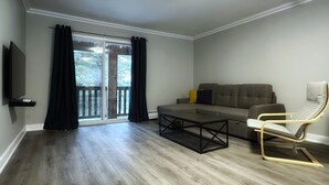 A modern living room with a sectional sofa, a coffee table, a TV mounted on the wall, and a sliding glass door leading to an outdoor area. - Pinedale Inn (Gravenhurst)