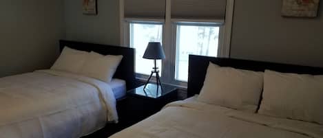 Een hotelkamer met twee bedden, een nachtkastje met een lamp en een raam met jaloezieën.