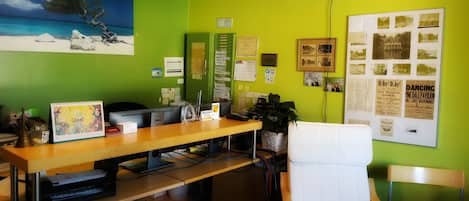 A reception desk with a computer, a calendar, and a plant. There is a chair and a desk lamp.