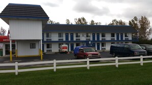 Un motel à l’extérieur blanc et bleu, doté de nombreux balcons et d’un parking où sont stationnés plusieurs véhicules.