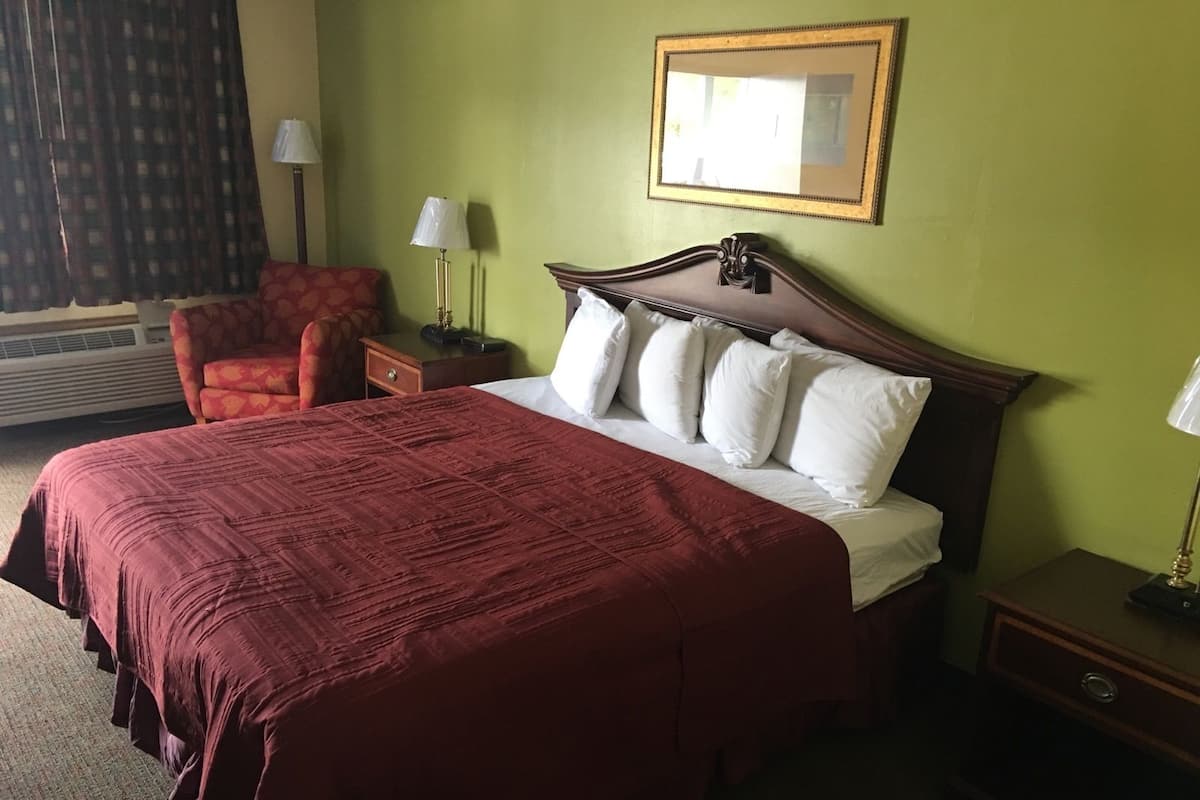 A hotel room with a large bed, a chair, two bedside tables, and a mirror on the wall.