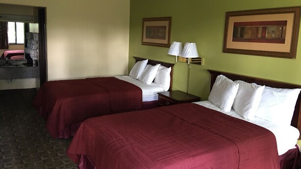 Une chambre d’hôtel avec deux lits, chacun recouvert d’une couverture rouge et agrémenté d’oreillers blancs, une table de chevet, une lampe et deux tableaux encadrés accrochés au mur.