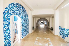 A hotel corridor with a geometric patterned floor, white walls, and blue decorative elements. - Hotel Tmk Marine Beach (Djerba Midun)