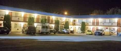 Un motel con varios espacios de estacionamiento, un área de estacionamiento techada y un edificio con techo azul.