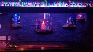 Un espace bar avec un mur en pierre, des bouteilles éclairées et un panneau néon.